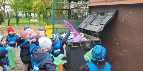Powiększ grafikę: Dzieci z grupy 4 wrzucają do śmietnika pełne worki nazbieranych śmieci.