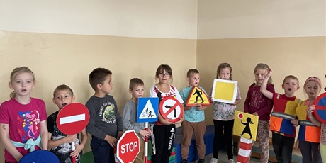 Powiększ grafikę: W  sali stoi  grupa  dzieci  trzymająca  znaki  drogowe.