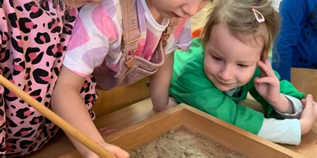 Powiększ grafikę: Dziewczynki szukają jajek dinozaurów zakopanych w piasku.