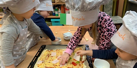Powiększ grafikę: Ubrane w kucharskie czapki dzieci komponują swoją pizzę.