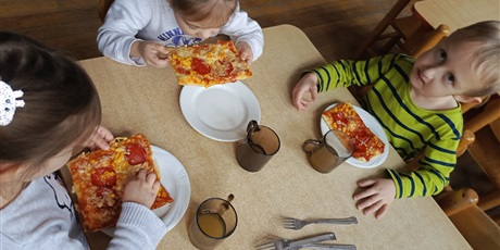 Powiększ grafikę: Dzieci jedzą pizzę.