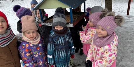 Powiększ grafikę: Dzieci  z zaangażowaniem pomagają ptakom, wsypując karmę do karmnika.