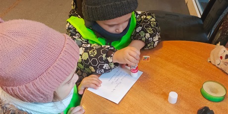 Powiększ grafikę: Dzieci naklejają pocztowy znaczek.